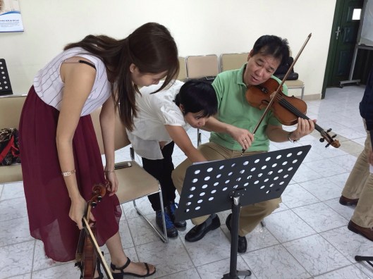 Kimngoc Tran discusses a detail with violinists Khanh Linh and Pham Truong Son.