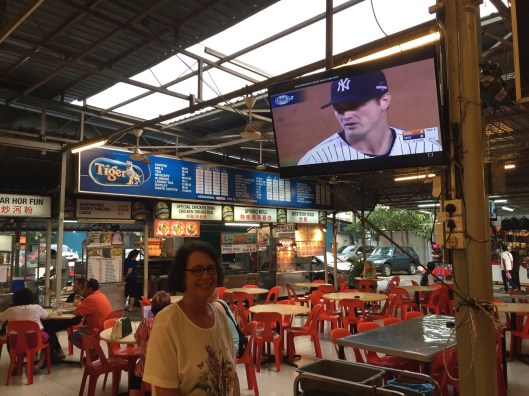 Jan in the Batu Ferringhi food court, and yes that's MLB baseball on behind her