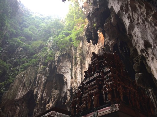 A view of shrine and rock leading to a natural skylight from above and dripping streams of water.